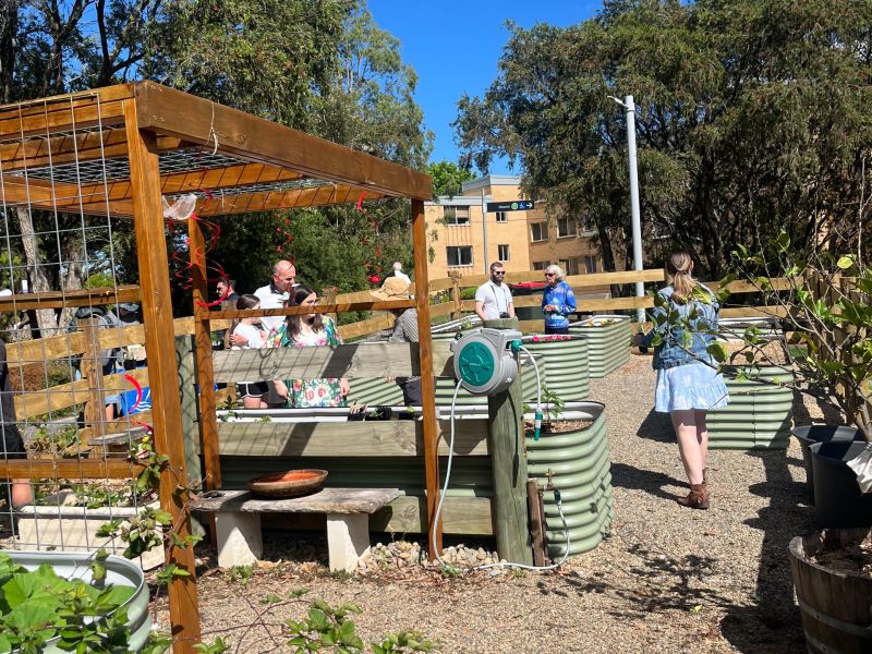 People walking around raised garden beds and wooden hanging garden structure