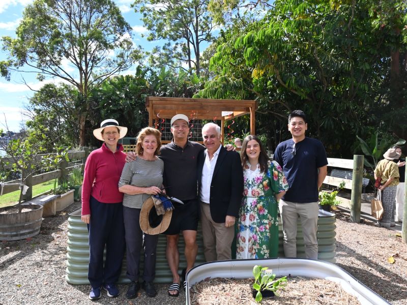 Group of people posing in front of a garden bed on a sunny day