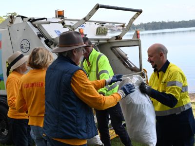 Group of volunteers handing rubbish to a garbage collector in front of a rubbish truck