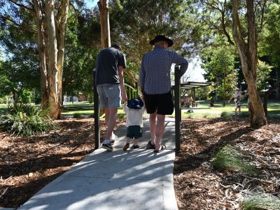 Two parents holding their childs hand walking along a path