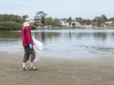 Woman walking along the shore picking up rubbish